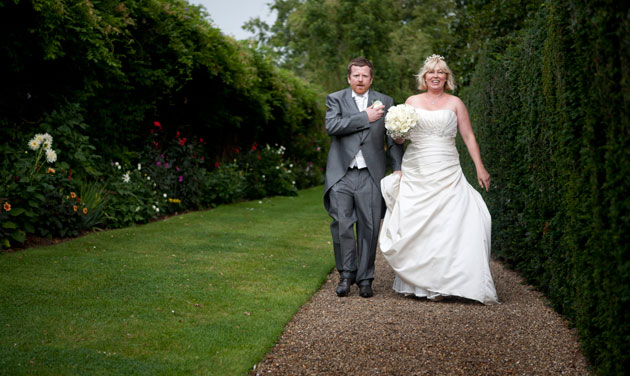 bride and groom walking on gravel path next to tall hedge at blake hall