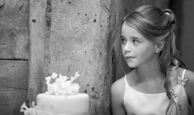 child bridesmaid leaning against wooden post in a barn next to a wedding cake