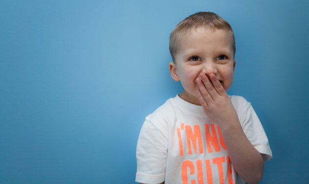 young boy with his hand to mouth against a blue background