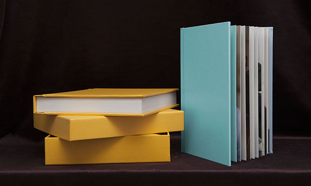 pile of yellow wedding albums next to a standing turquoise colour wedding album