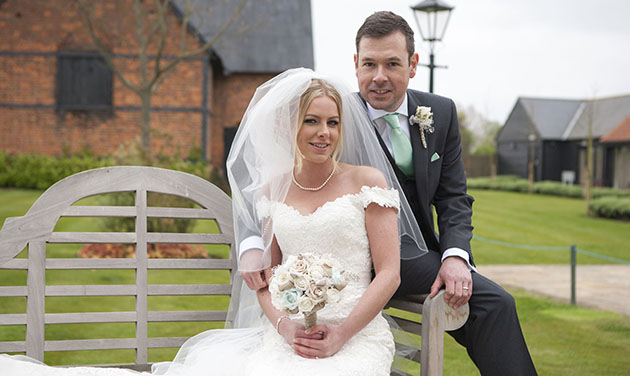 Bride sitting on bench groom sitting on side with barn in background at Channels Estate Essex