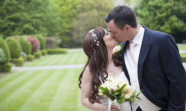 bride kissing groom with grounds of Theobalds Estate in background