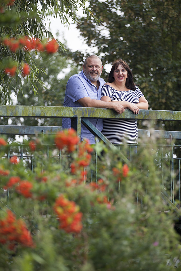 couple on bridge looking at camera with red flowers in foreground