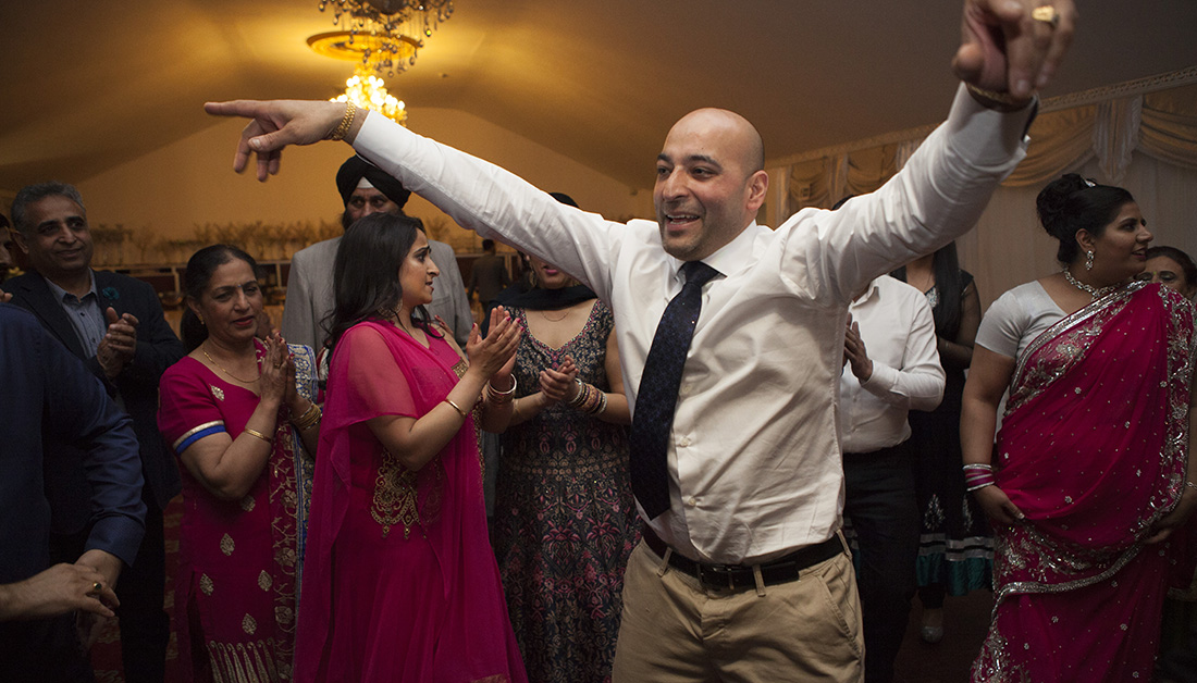 man in middle of dance floor with arms outstretched at an Indian party 