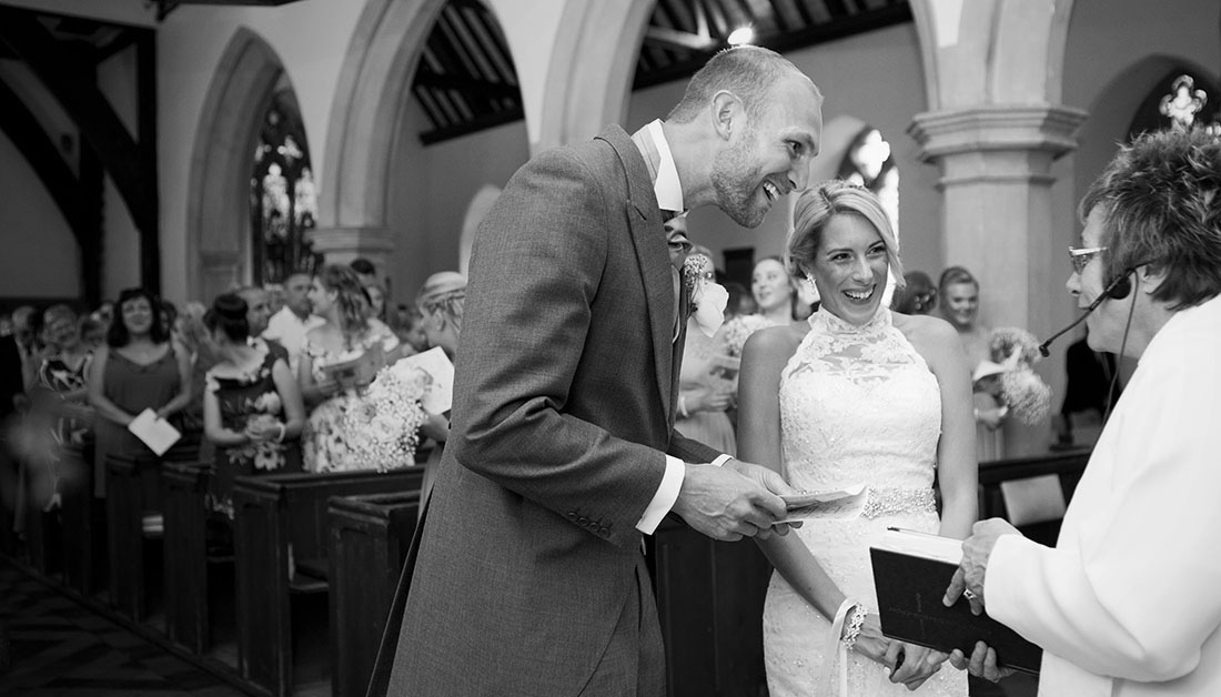 bride and groom laughing with vicar during wedding ceremony in an Essex church