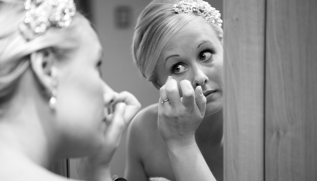 bride looking in mirror and putting on eye make up 