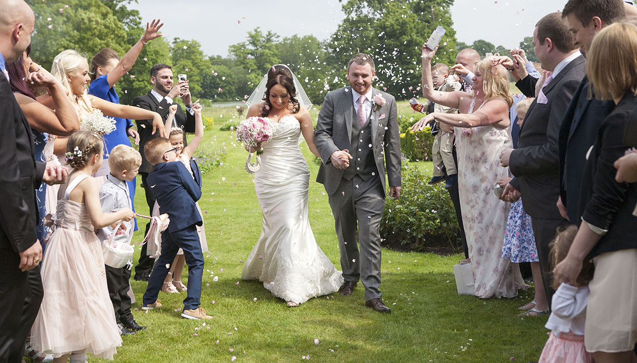 bride and groom walking between two rows of people as they throw confetti
