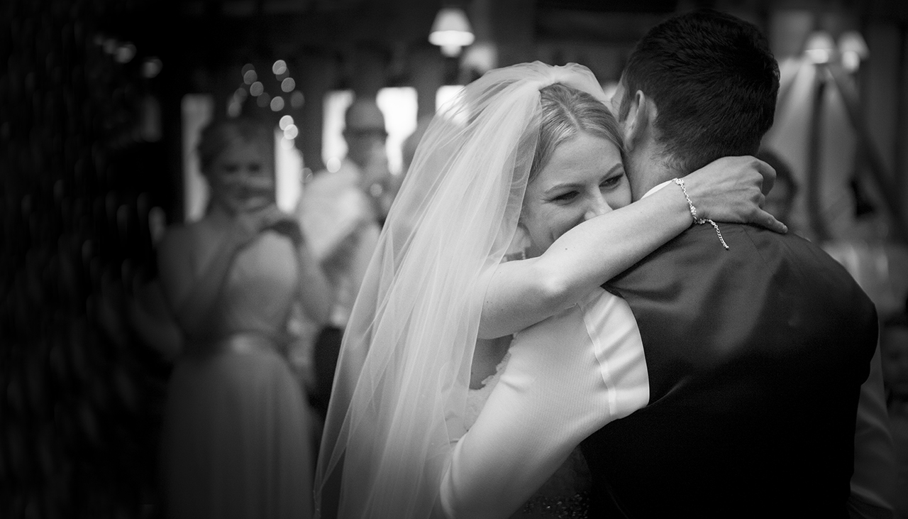 bride with veil laughing with her arms around the groom's neck during a wedding first dance