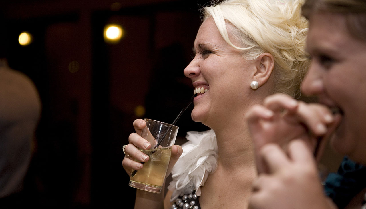 girl holding a drink and laughing at a party against black background 