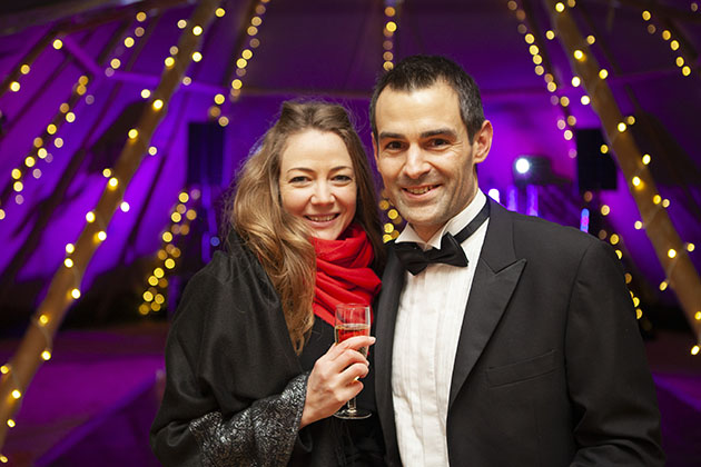 Two guests at black tie party looking at camera with sparkling lights in the background