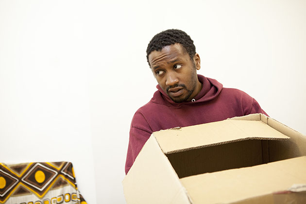Actor Kieron Mieres in rehearsal holding an empty cardboard box looking to the side