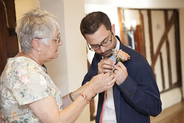 Groom having help fixing his buttonhole 