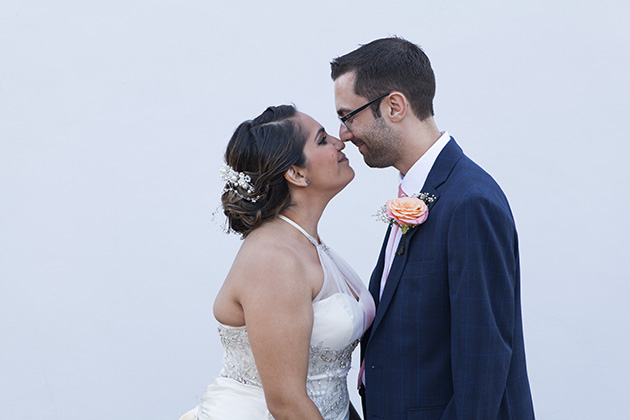 Bride and groom facing each other with their noses together standing by a white wall