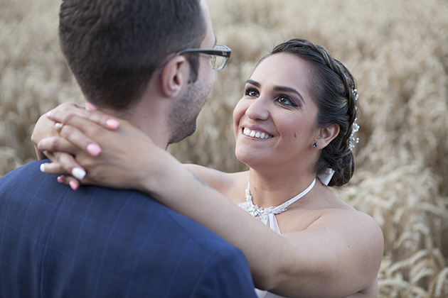 Close up of bride with her hands around the neck of the groom with a field of wheat in the background