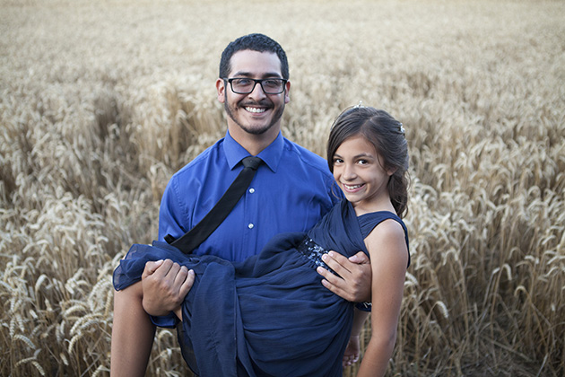 Wedding guest holding young bridesmaid in his arms with field of wheat in the background