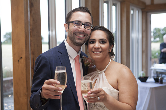 Bride and groom holding out glasses of champagne and looking at camera