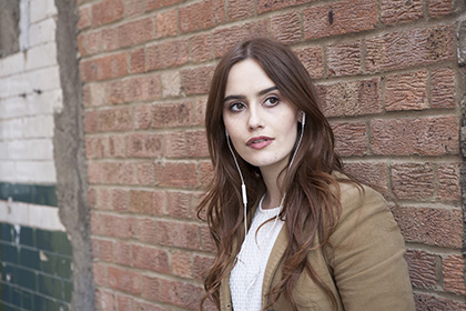 Portrait of young woman leaning against old brick wall listening to music on headphones