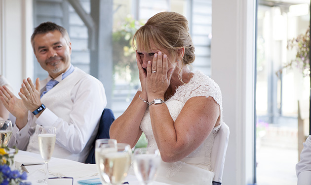 Emotional bride with hands on her face during wedding speeches