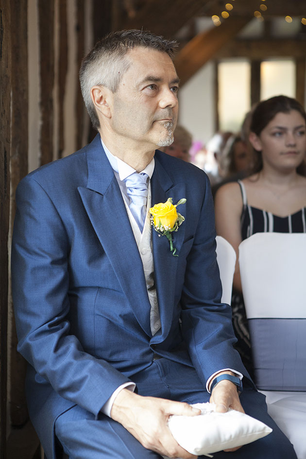 Best man sitting at wedding ceremony holding rings on a cushion