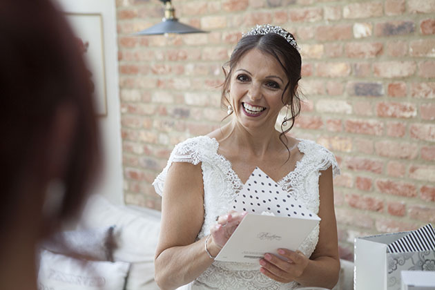 Bride smiling whilst opening a greetings card with a brick wall in background