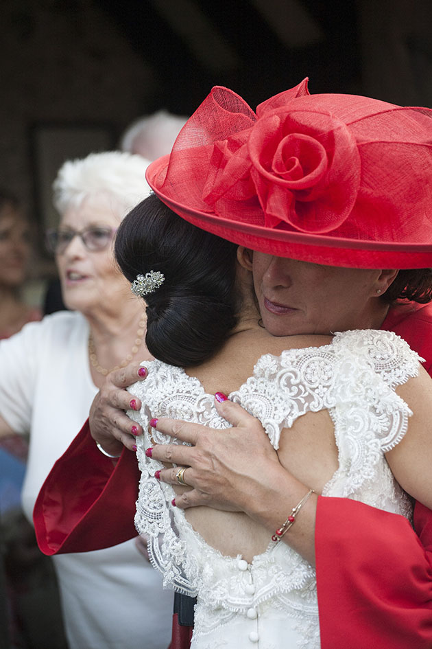 Woman wearing large red hat hugging bride