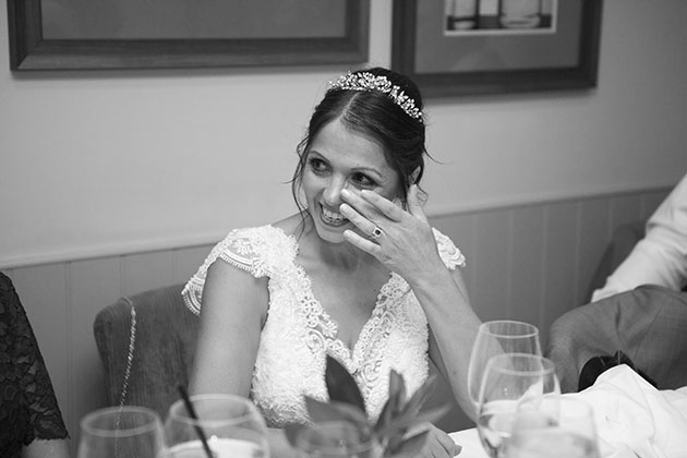 Bride sitting at table and wiping her eye during speeches at wedding reception