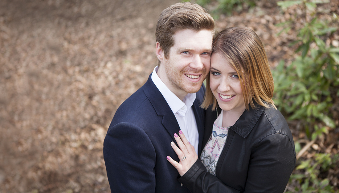 engaged couple in Essex woodland holding each other and looking at camera