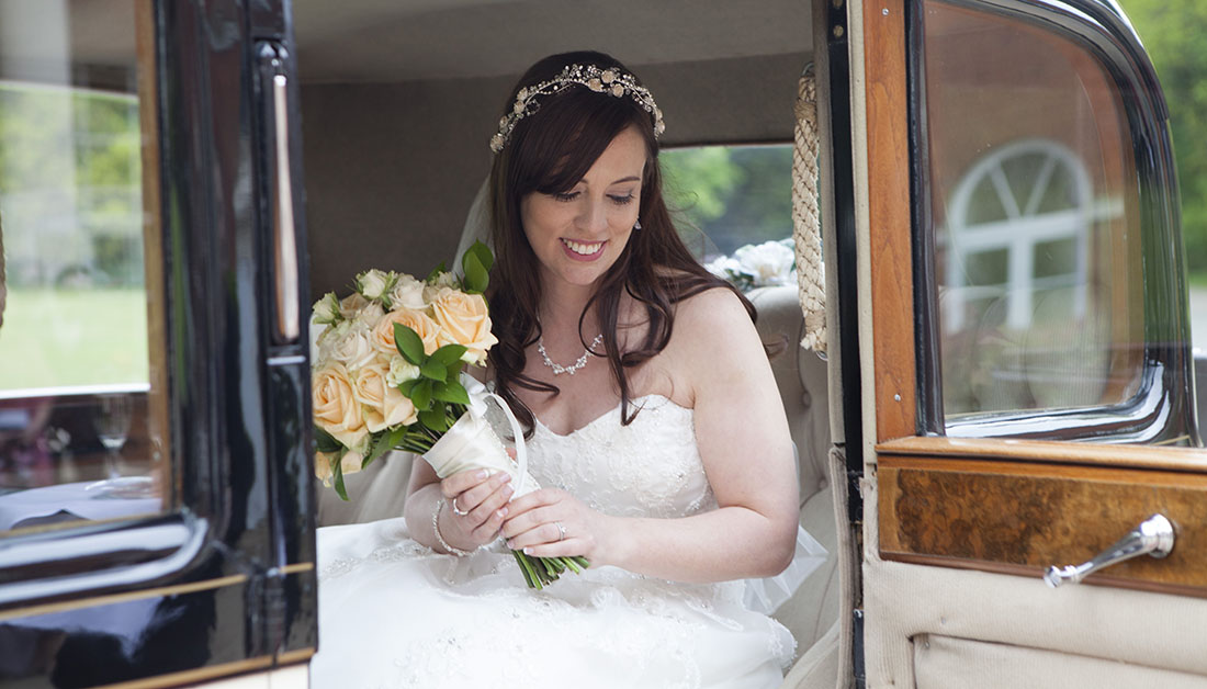 bride in doorway of vintage rolls royce holding bouquet of yellow flowers