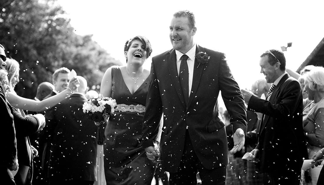 confetti being thrown over bride and groom as they walk between the wedding guests