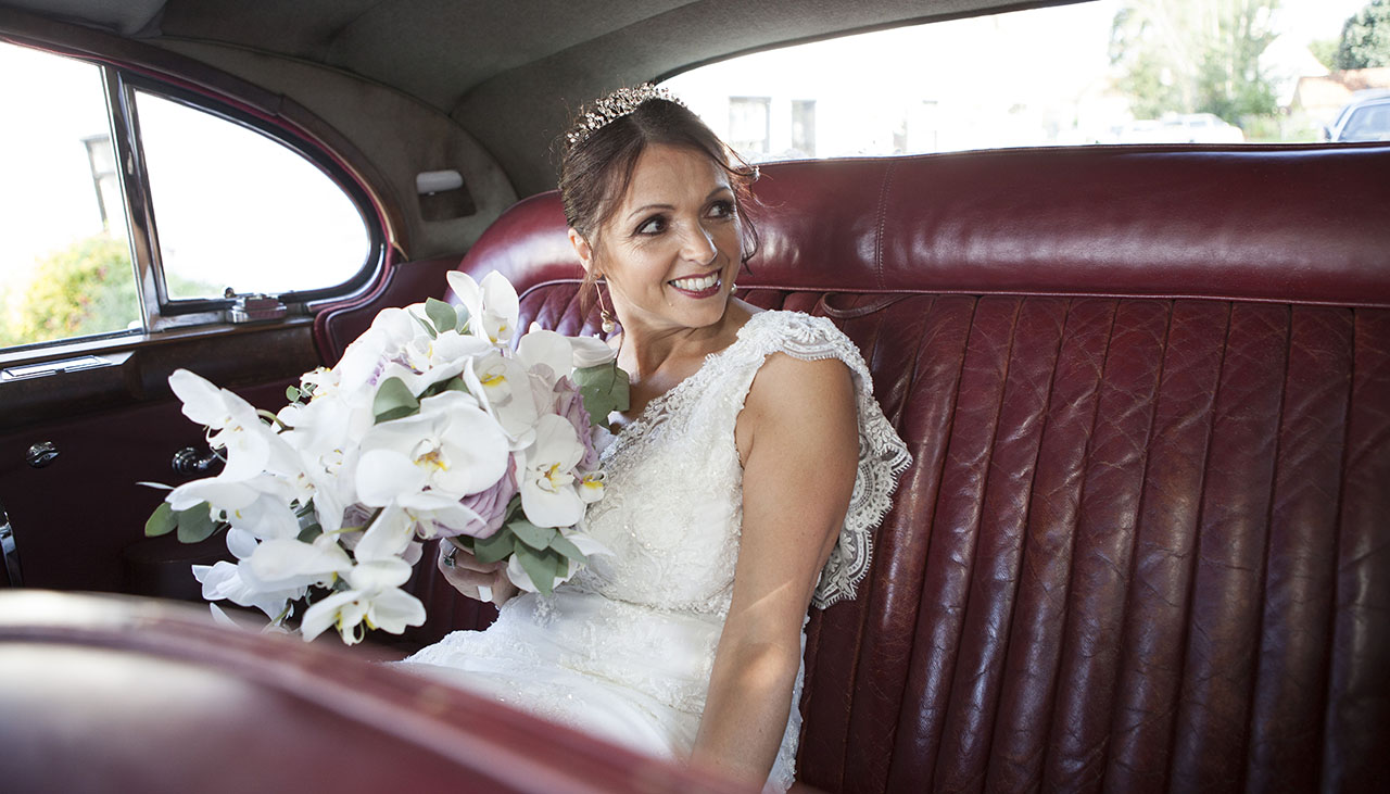 bride with bouquet of flowers on red leather back seat of car looking to the right