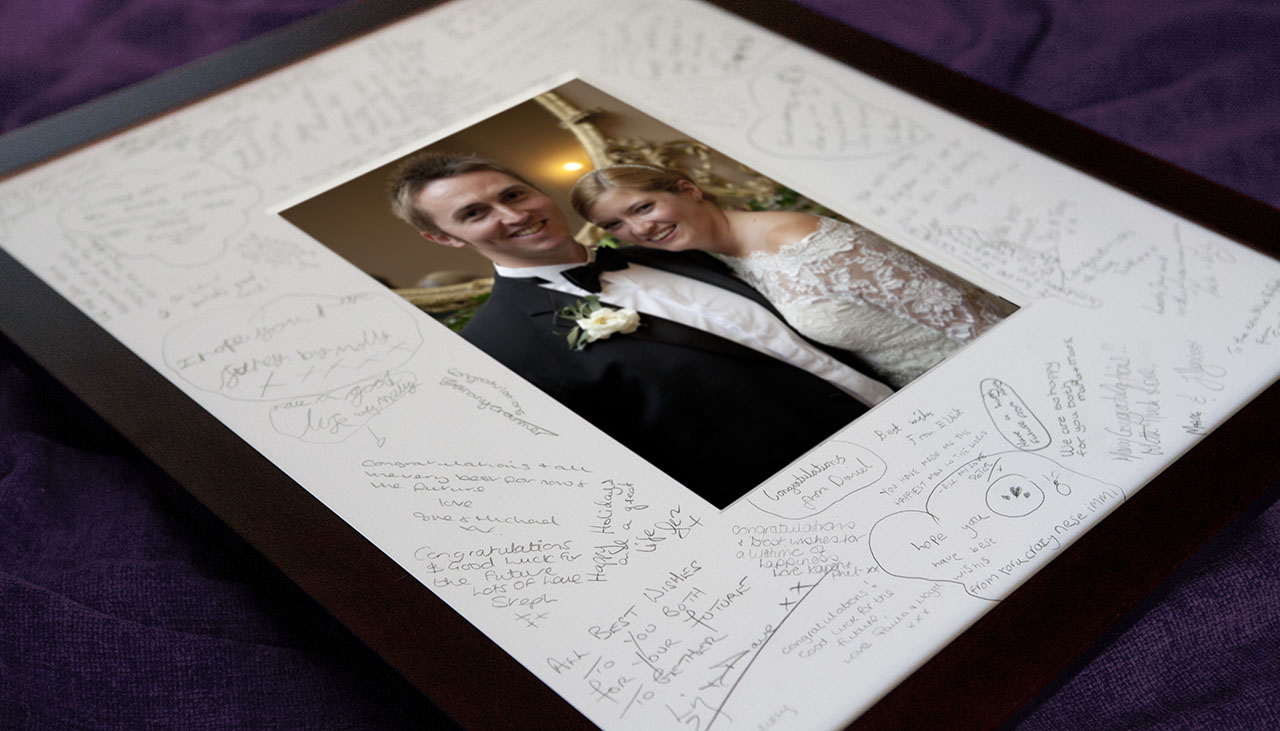 photo of recently married couple in a picture frame with a wide mount that guests have signed