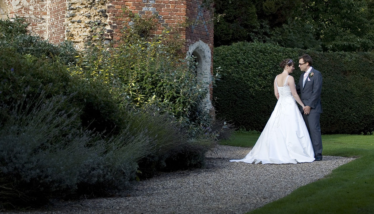 bride and groom holding hands at the foot of the tower in the grounds of Leez Priory Essex