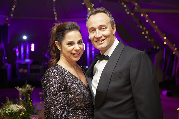 Two guests at black tie party looking at camera with coloured lights in the background