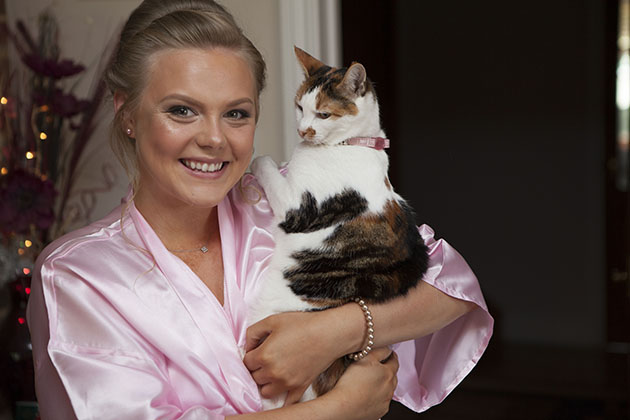 bridesmaid in a pink dressing gown holding cat and looking at camera