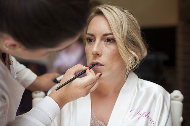 bride having lipstick applied during bridal preparations at home