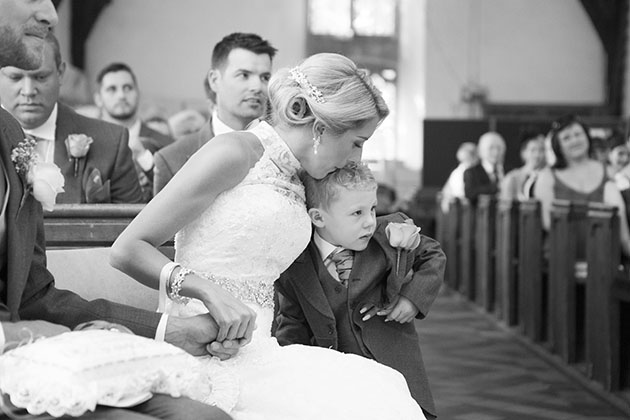 bride kissing the head of her young son during the wedding ceremony at Roxwell church