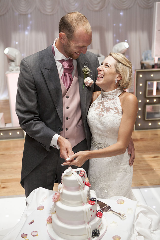 bride and groom cutting wedding cake with arms around each other and laughing