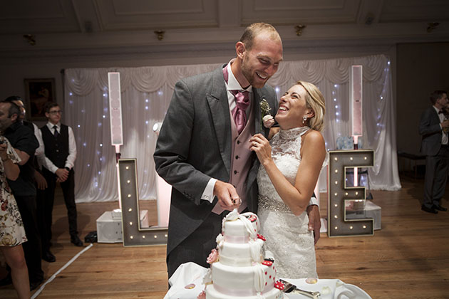 bride and groom cutting wedding cake with arms around each other and laughing