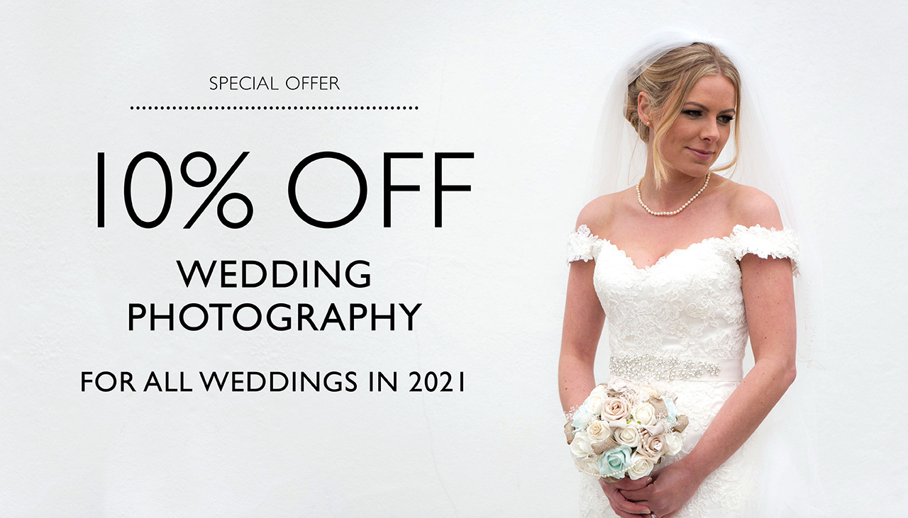 bride wearing white dress holding bouquet standing against white wall and looking to the side