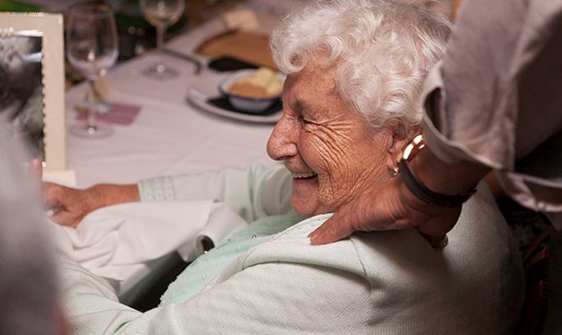 Old woman at dining table with a hand on her shoulder