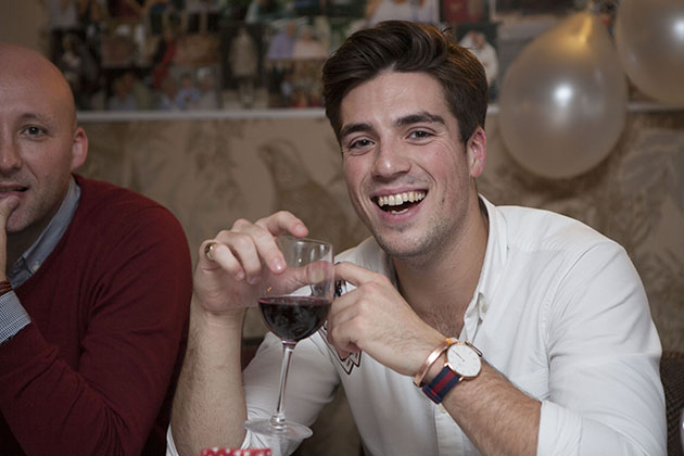 Young man holding glass of wine, looking at camera and laughing