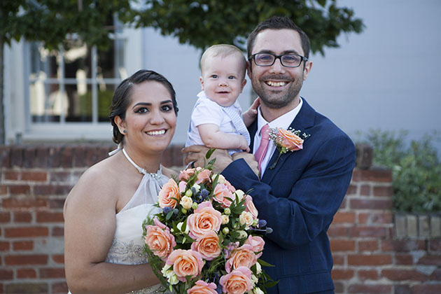 Bride and groom holding baby and all looking at camera