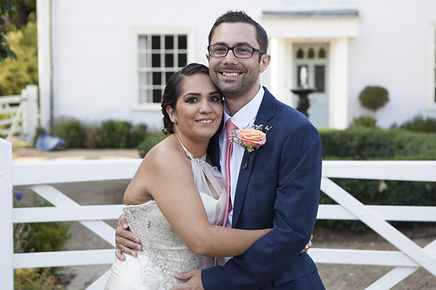 Bride hugging groom in front of a gate to a farm house