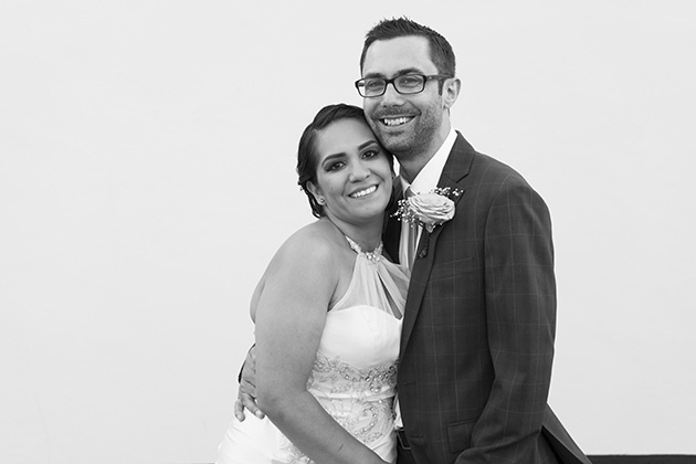 Bride and groom hugging each other standing by a white wall