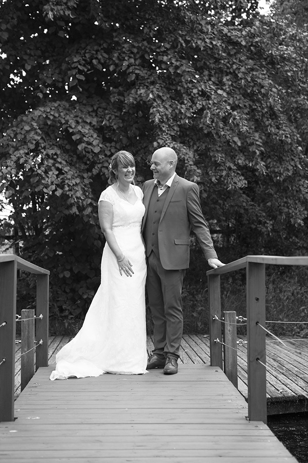 Natural portrait of bride and groom laughing on bridge over a pond