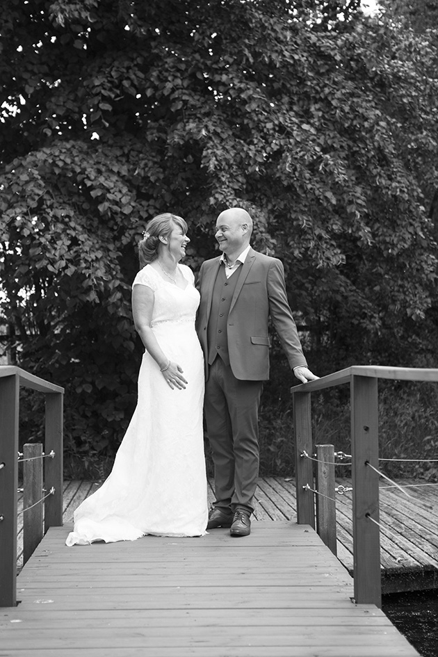 Natural portrait of bride and groom laughing on bridge over a pond
