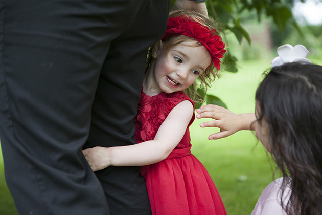 Young girl in red dress and red headband with arms around leg of adult