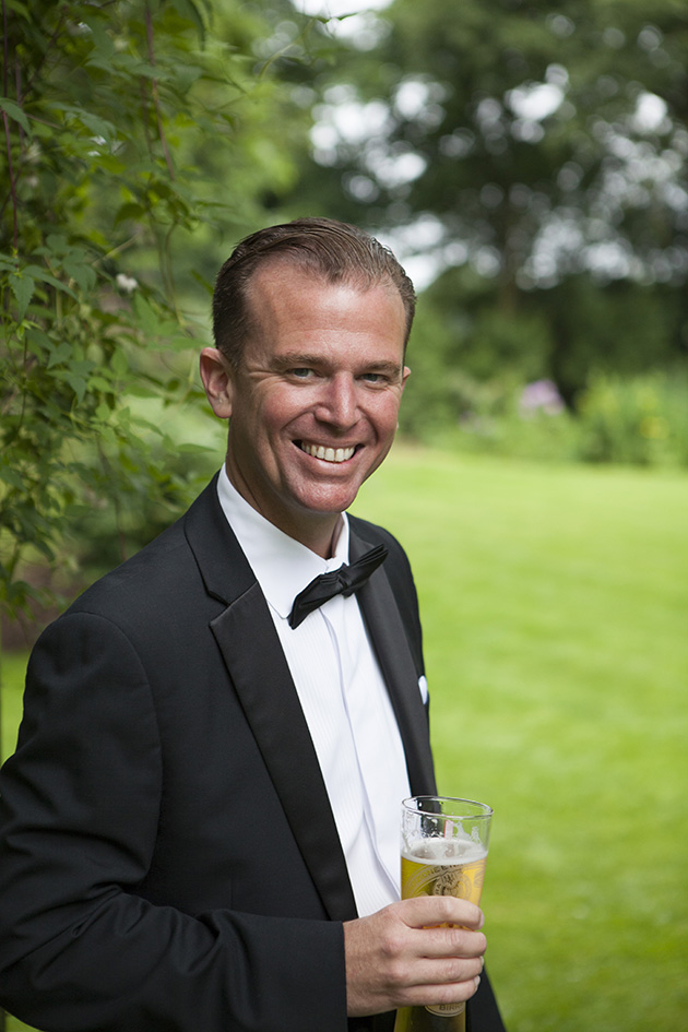 Man in black tie holding pint of lager in hotel garden
