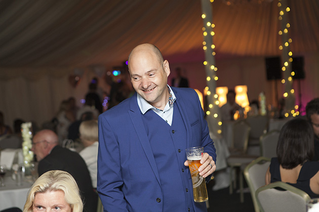 Groom holding a pint of beer and talking to weddings guests