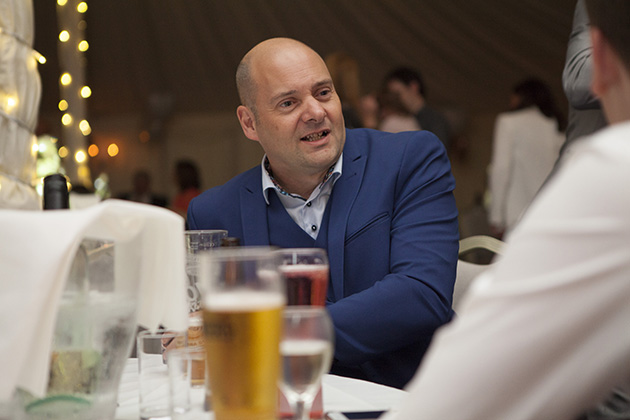 Groom sitting at table talking to wedding guests